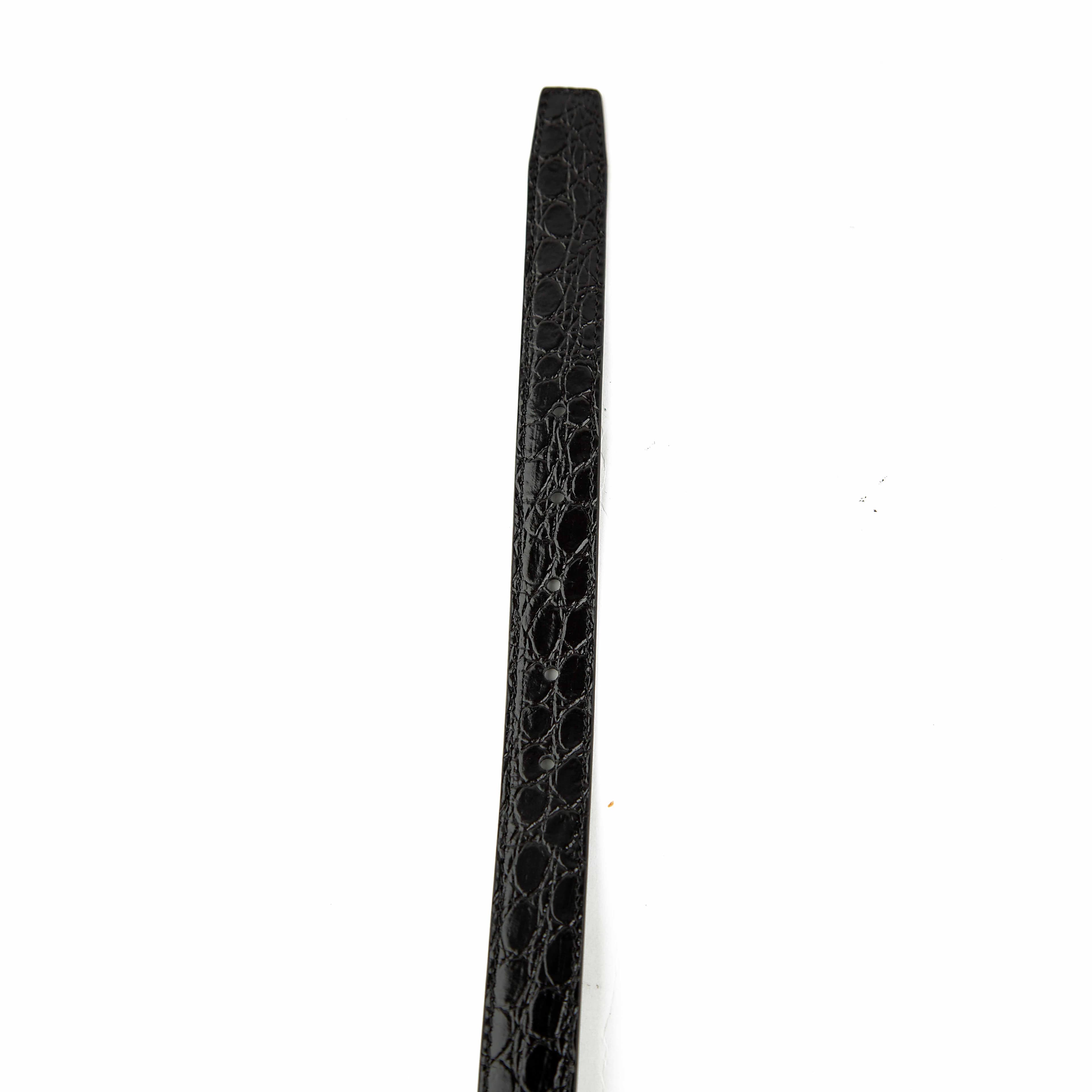 This elegant accessory is a masterclass in understated luxury, featuring a smooth, semi-matte black calfskin leather strap.