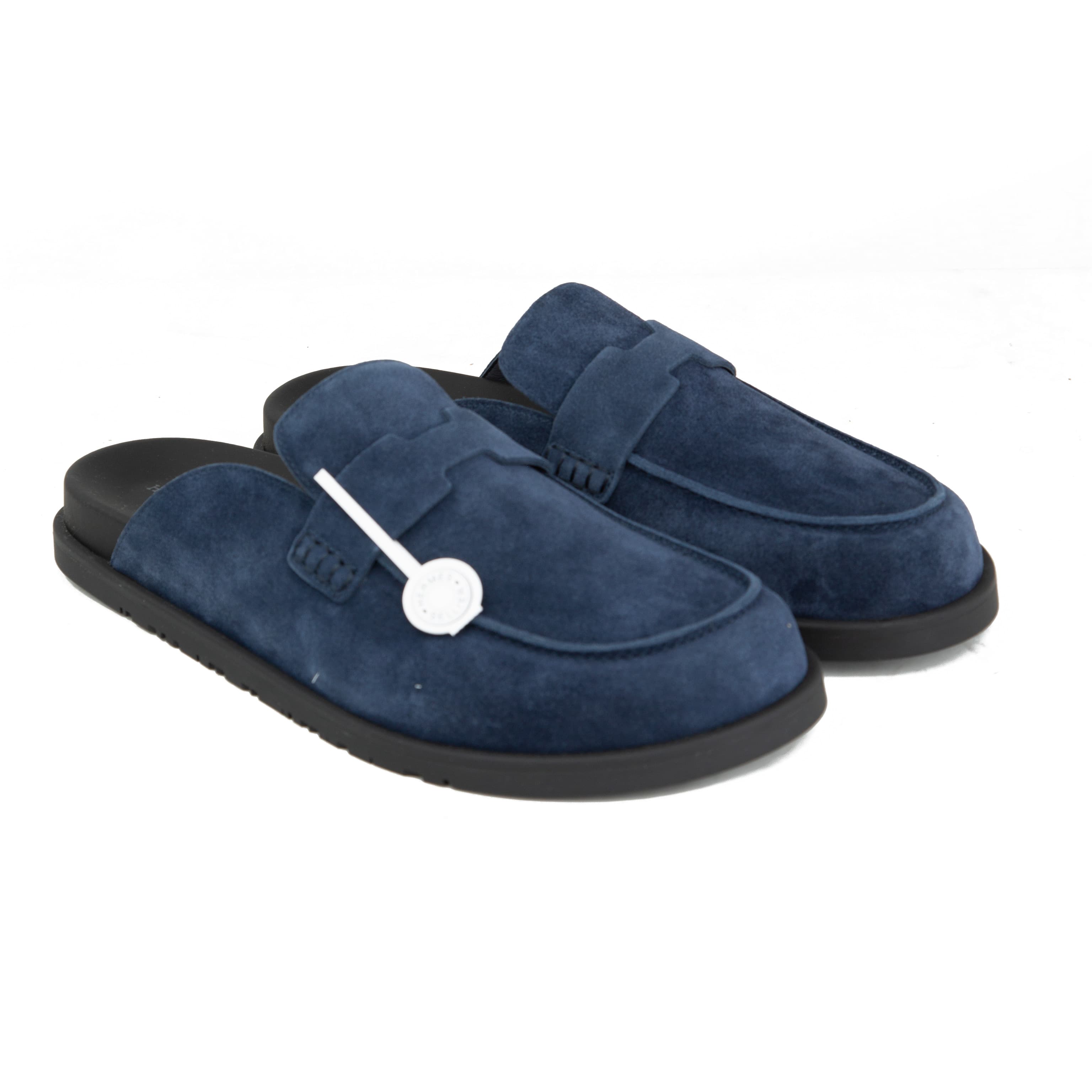 Pair of navy blue suede Hermès Ancora mules with tonal H strap and black rubber soles on a white background.