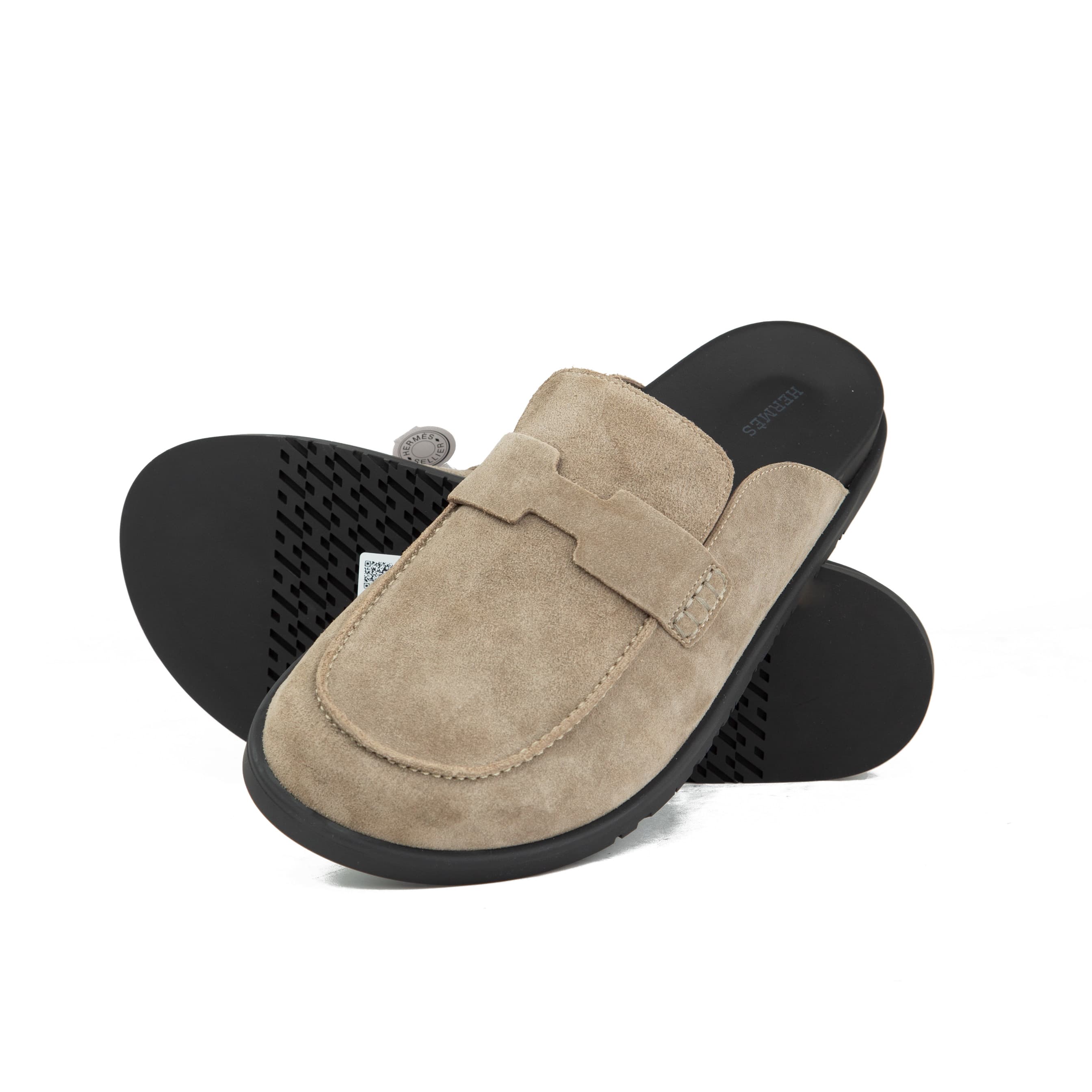 Pair of warm taupe Etoupe suede Hermès Ancora mules with tonal H strap and black rubber soles on a white background