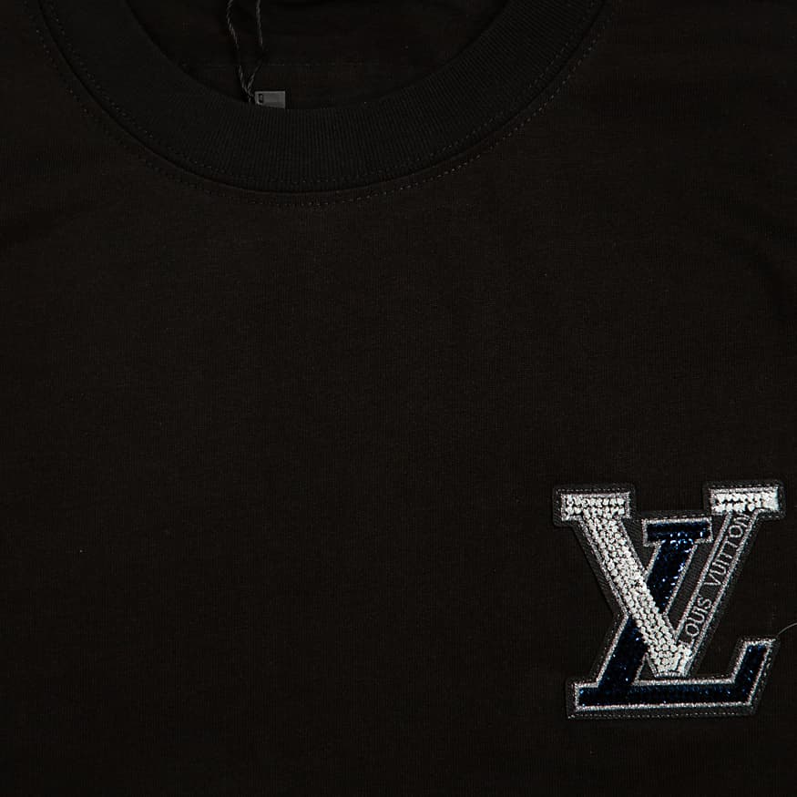 A sleek, classic black, short-sleeved, crew-neck t-shirt. It features a small, eye-catching appliqué patch on the left chest.
