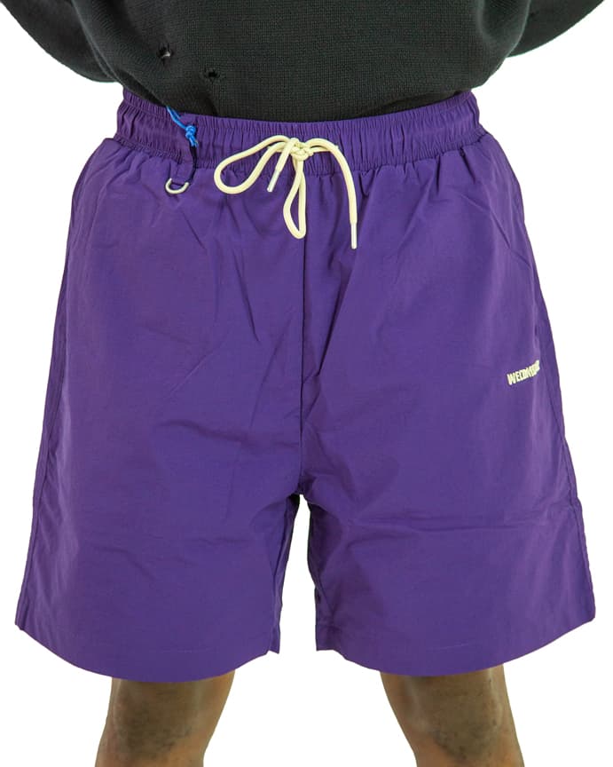 Purple nylon swim shorts with elastic waistband and drawstring closure, shown on a person against a white background.