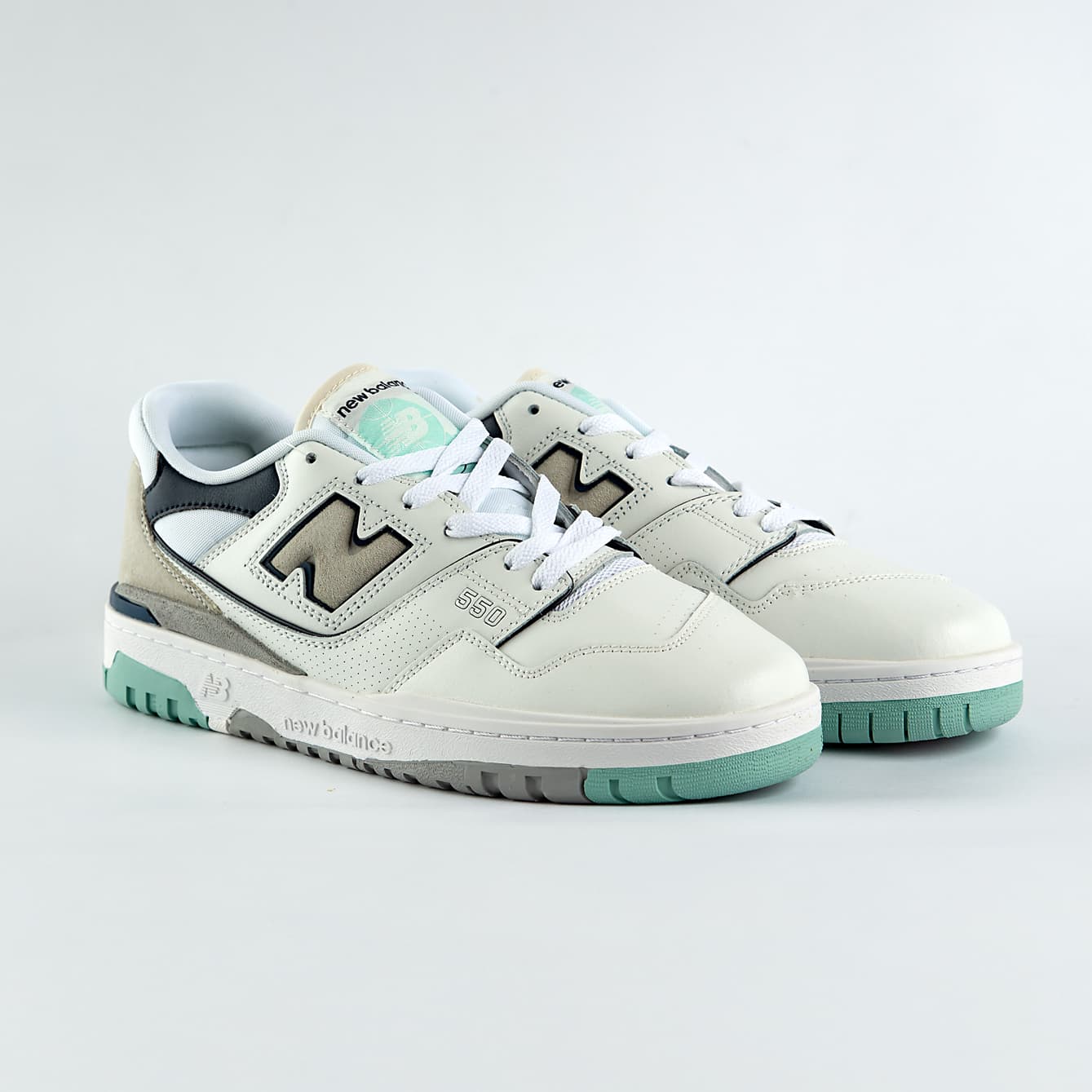 New Balance 550 sneakers in off-white with mint green, taupe, and gray accents. A retro low-top shoe for men and women.