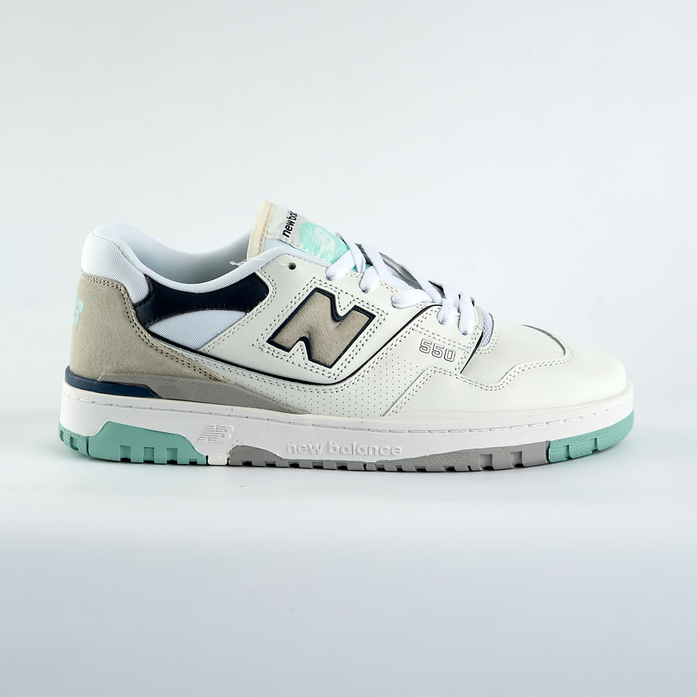 New Balance 550 sneakers in off-white with mint green, taupe, and gray accents. A retro low-top shoe for men and women.