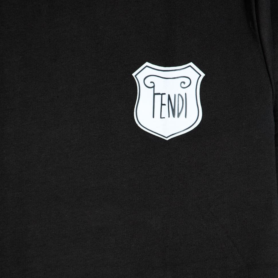 This is a classic black crew-neck t-shirt featuring a white, shield-shaped patch with the 'FENDI' logo displayed prominently on the chest. It's a versatile piece of designer casual wear.
