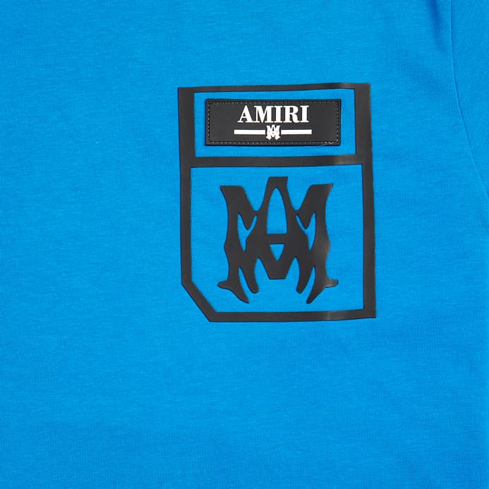 Bright blue Amiri unisex t-shirt with a black printed pocket logo featuring the AMIRI text and M monogram on the chest.