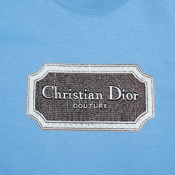 Light blue Christian Dior t-shirt with brown couture patch logo graphic on chest, luxury unisex style.