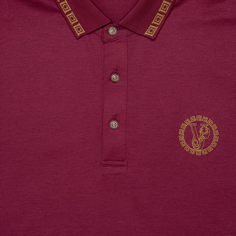 Maroon Versace polo shirt with gold Greek Key trim on collar/cuffs and embroidered Medusa crest, luxury short sleeve.