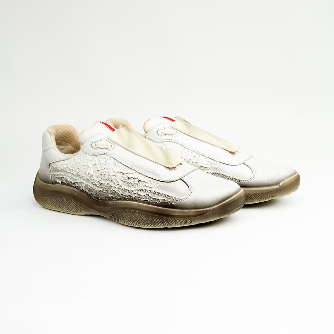 These high-fashion sneakers feature a unique white leather upper with a striking, textured cracked/distressed finish that fades dramatically into a darker, almost gradient effect at the midsole line, evoking the look of a receding glacier or ancient ice.