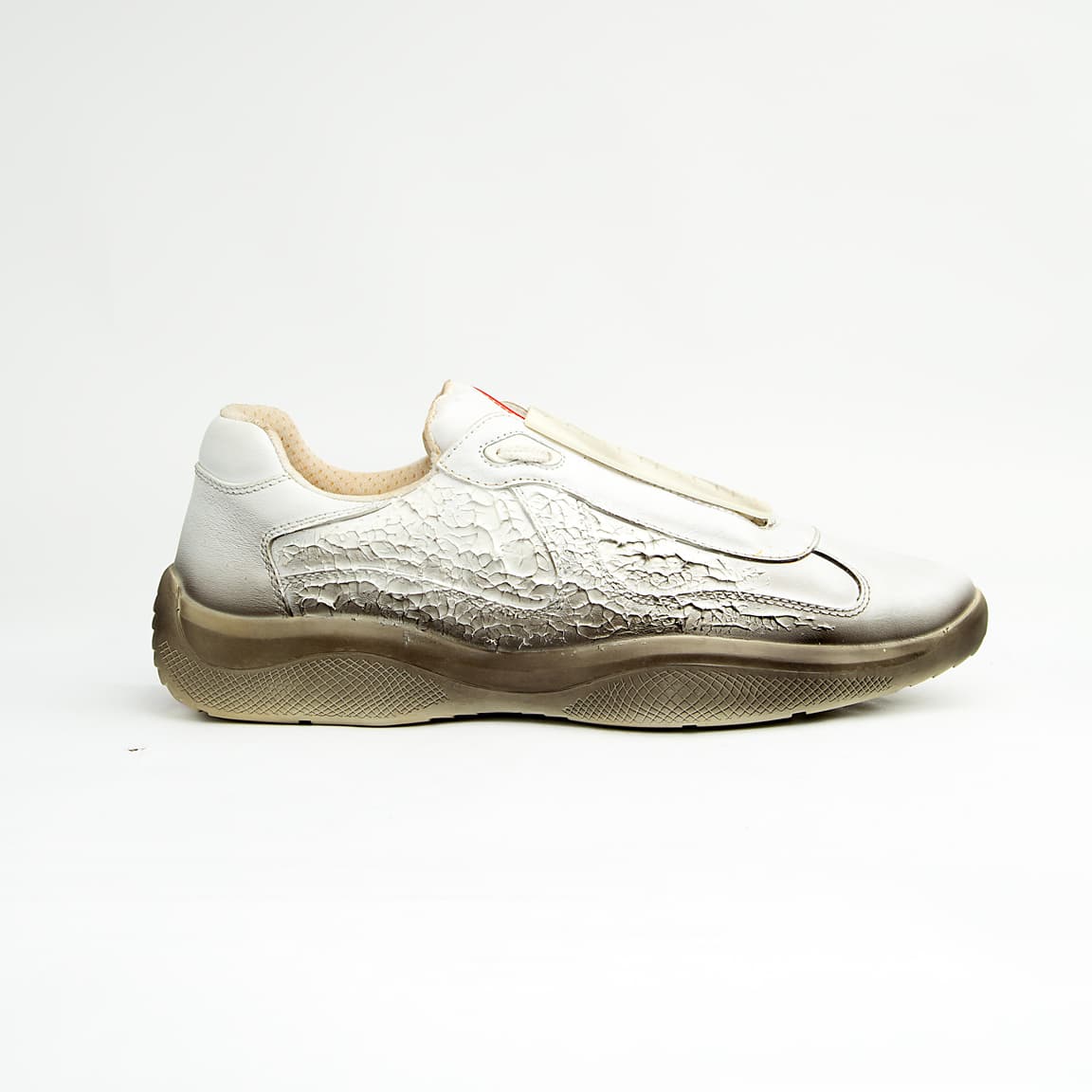These high-fashion sneakers feature a unique white leather upper with a striking, textured cracked/distressed finish that fades dramatically into a darker, almost gradient effect at the midsole line, evoking the look of a receding glacier or ancient ice.