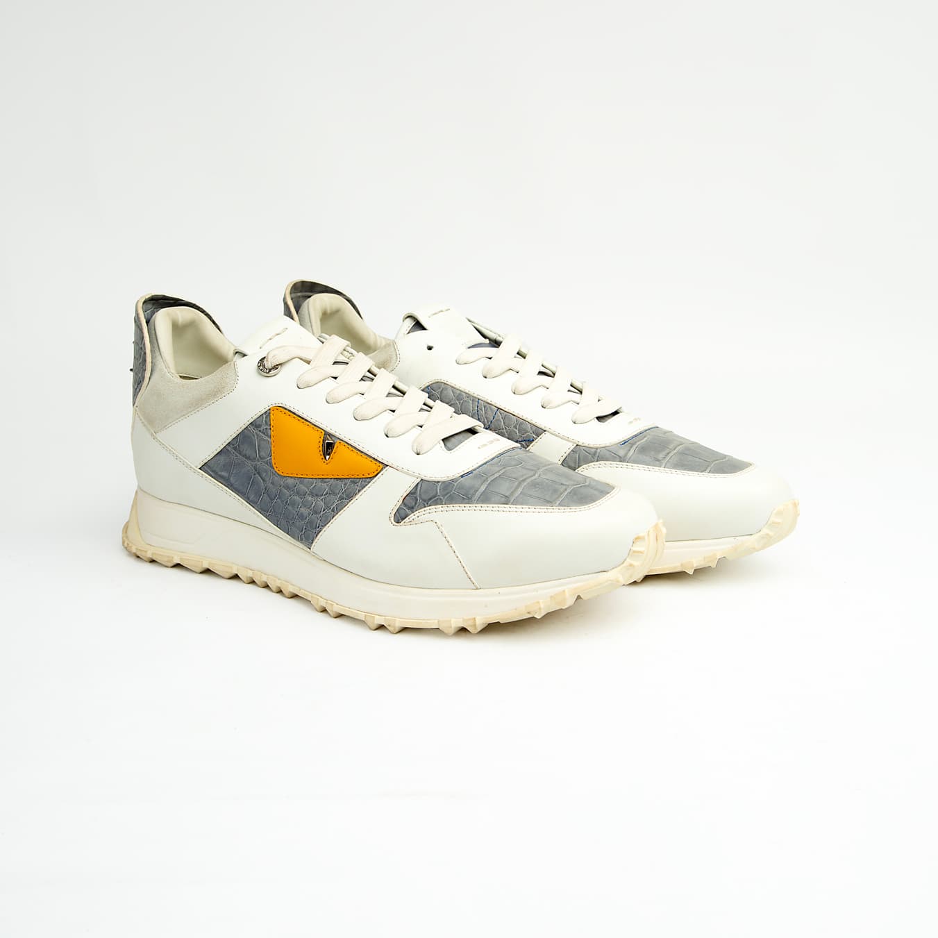 Crafted from premium leather, it features contrasting grey crocodile-embossed leather panels and a striking yellow-and-black triangular appliqué, reminiscent of a watchful eye.
