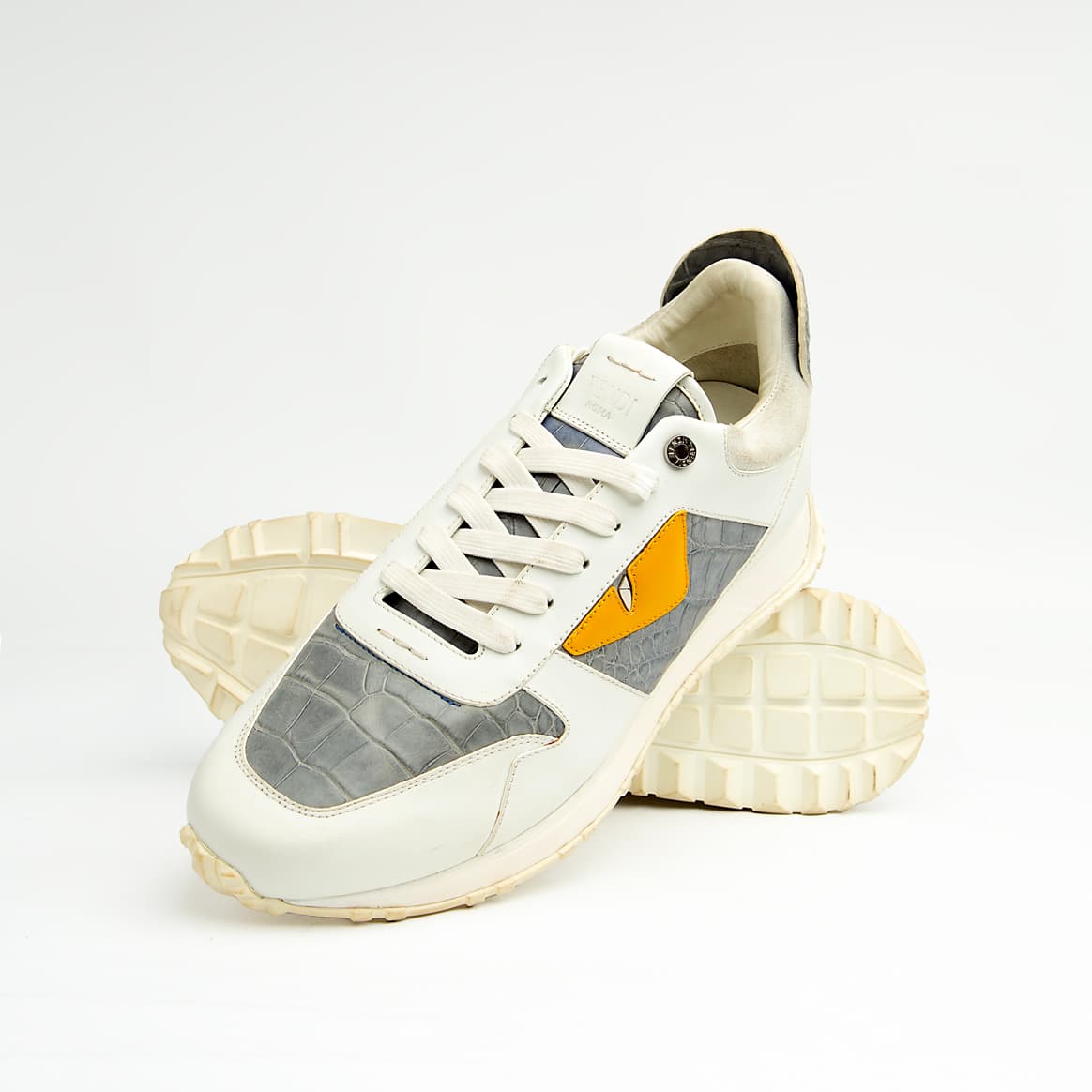 Crafted from premium leather, it features contrasting grey crocodile-embossed leather panels and a striking yellow-and-black triangular appliqué, reminiscent of a watchful eye.