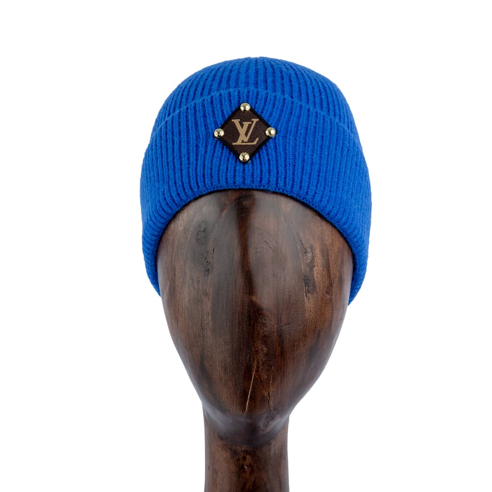 Blue knit beanie with monogram leather patch and gold studs, designed for style and warmth.