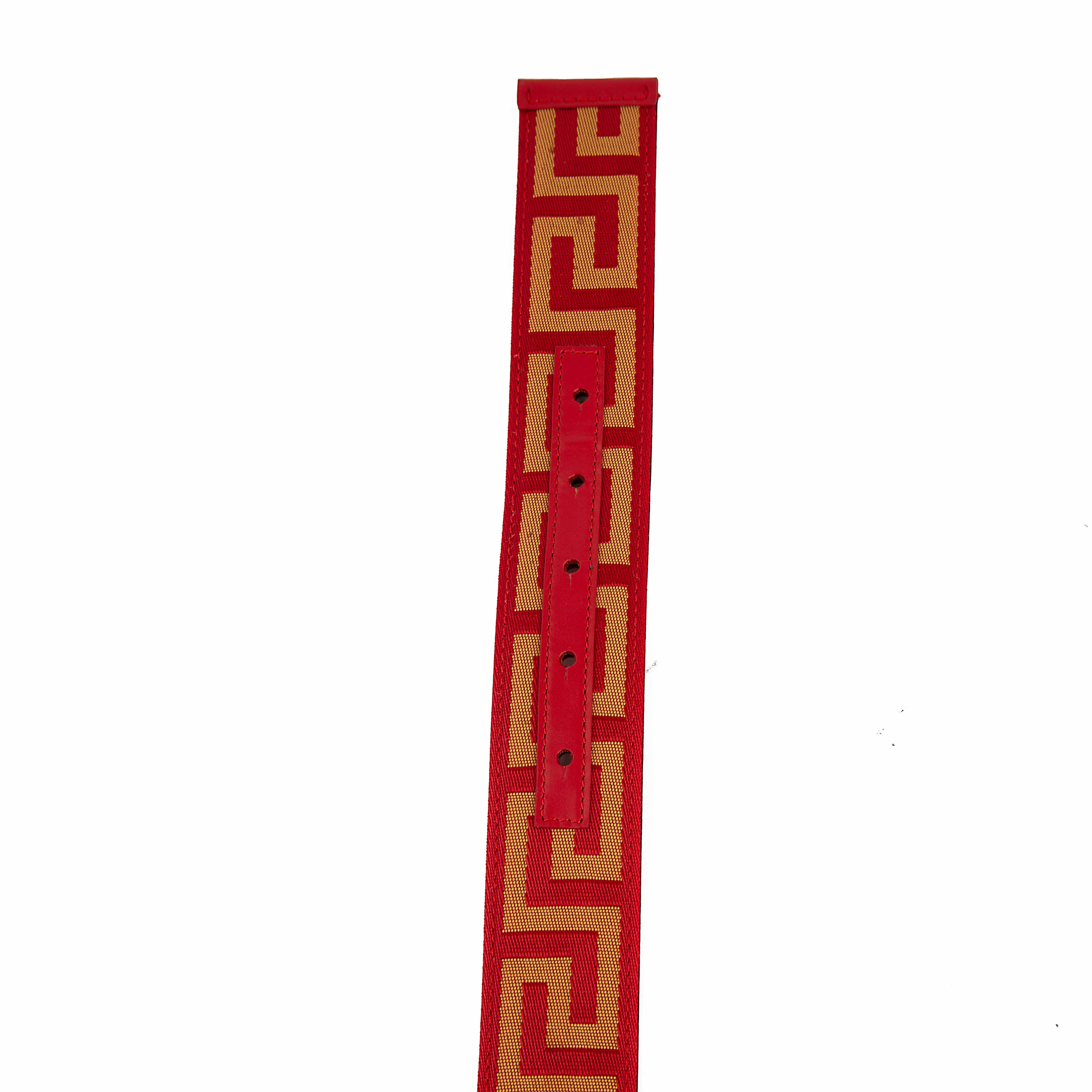 This belt is a masterclass in bold, unapologetic luxury. It features a vibrant scarlet red strap adorned with a continuous gold-tone Greca (Greek Key) motif, meticulously woven into a textured jacquard fabric.