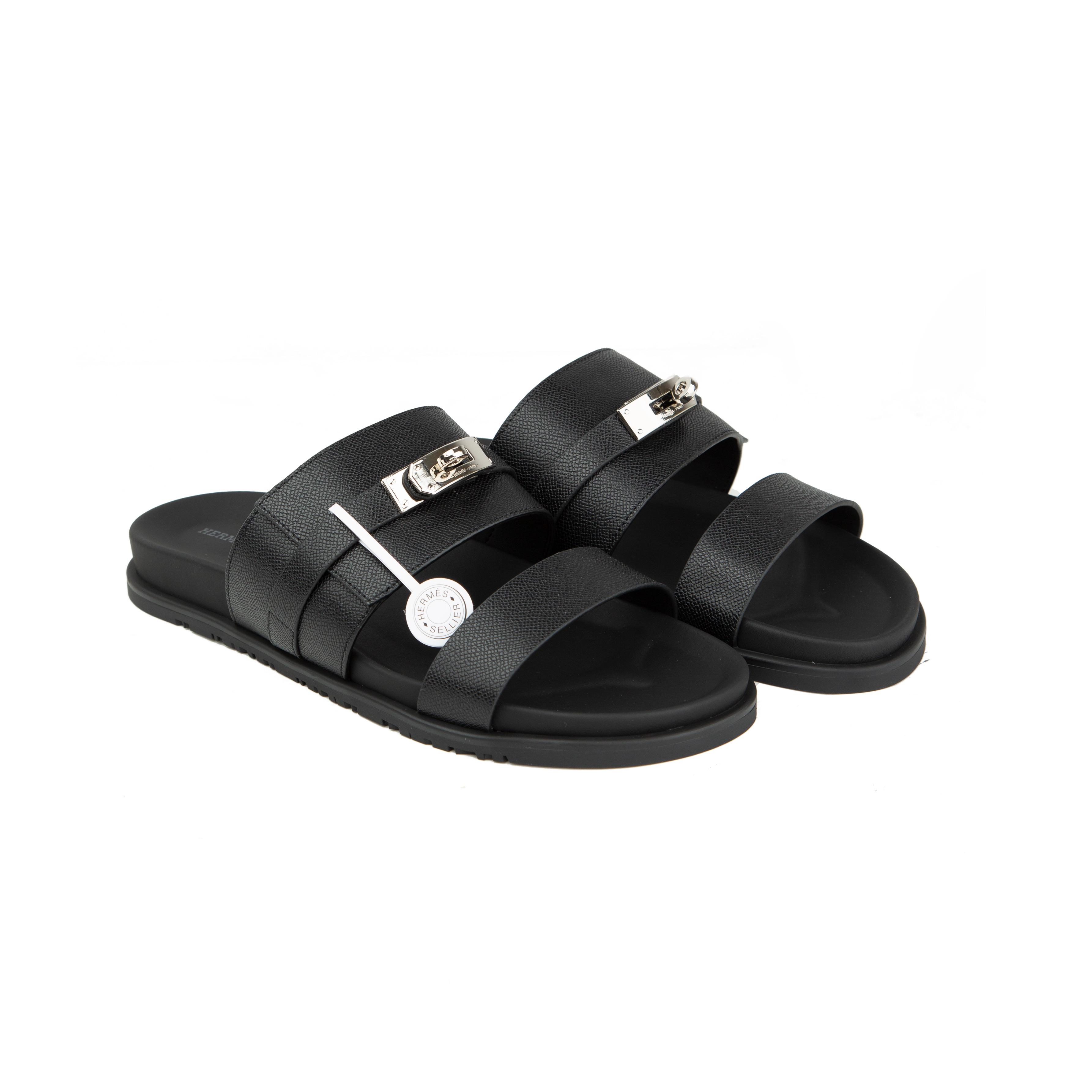 Black Hermès Chypre sandals in grained Epsom leather with silver Kelly buckle on a white background.