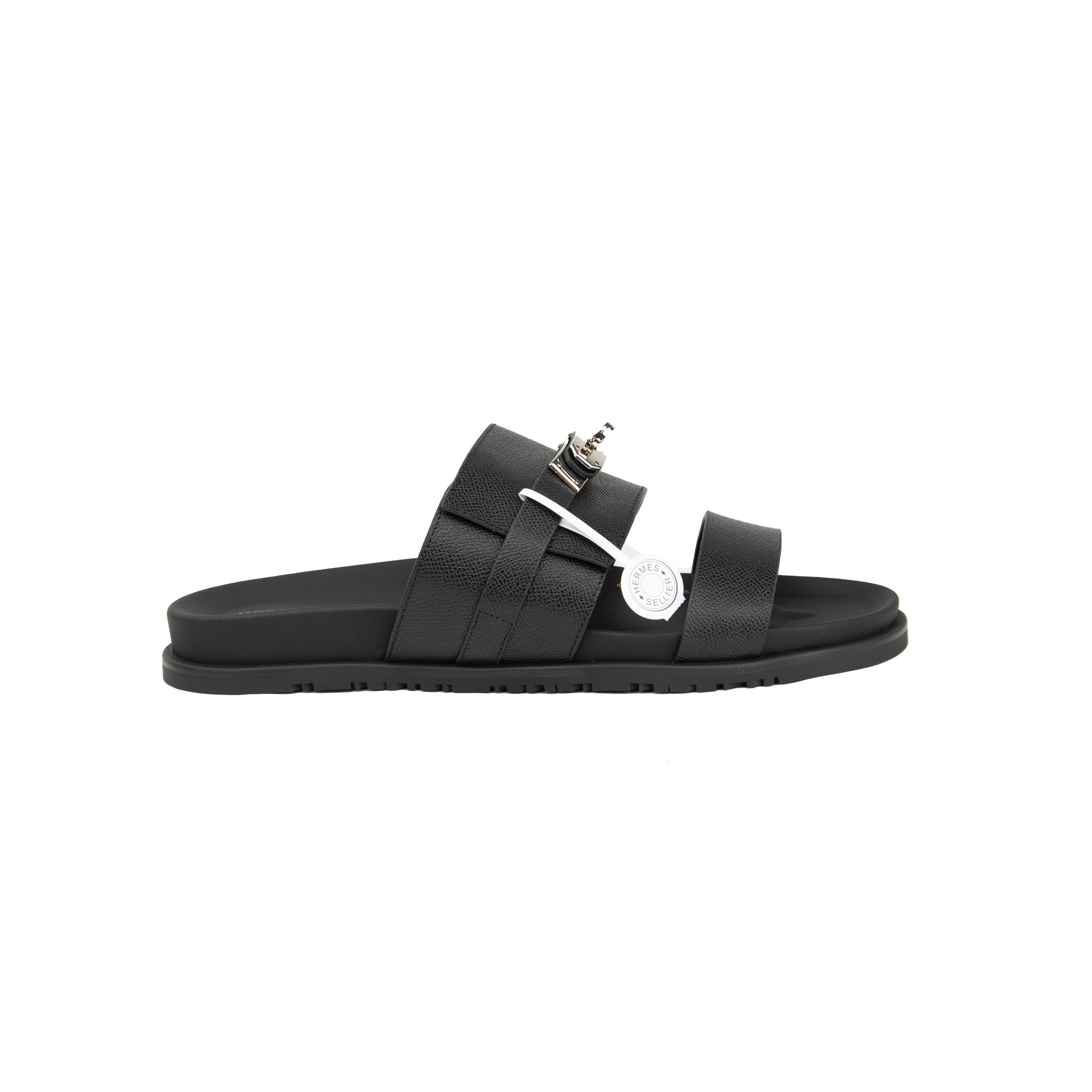 Black Hermès Chypre sandals in grained Epsom leather with silver Kelly buckle on a white background.