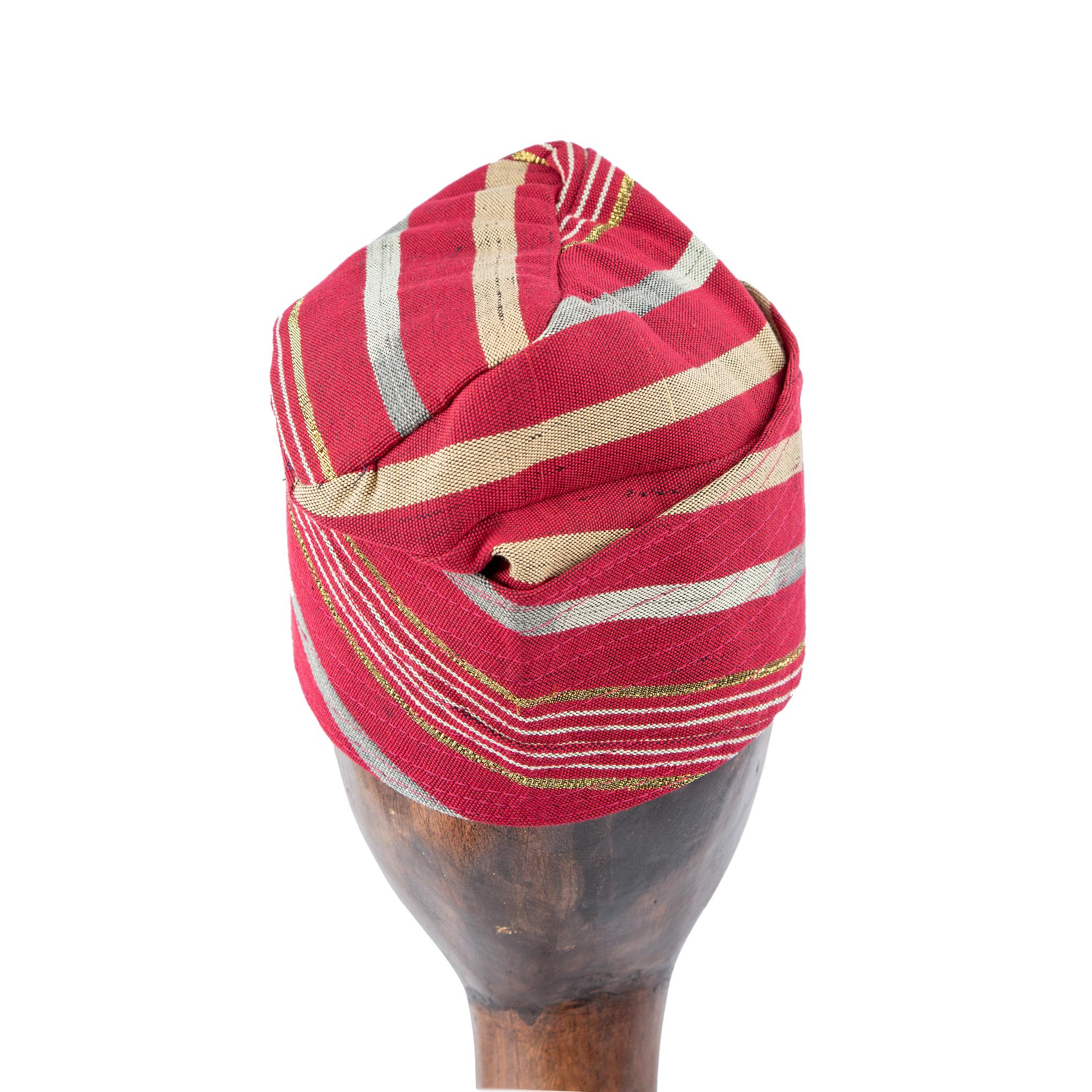 A Red and Gold Striped Yoruba Fila, meticulously folded and displayed on a wooden mannequin head.