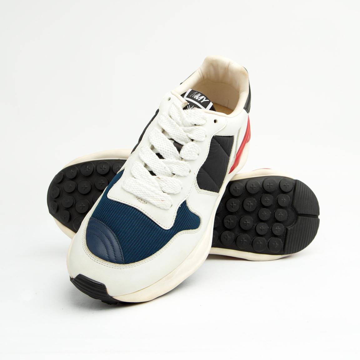 This bold sneaker features sophisticated color blocking with a base of pristine white leather, accented by rich navy blue mesh on the toe box and side panels, and black suede/nubuck near the laces.